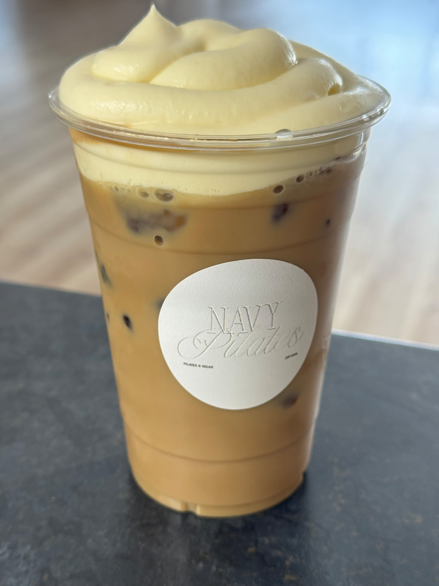 Iced latte with thick homemade cold foam whip beside a rolled black pilates mat